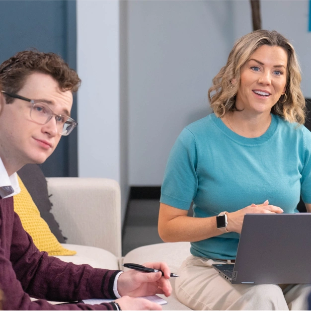 Two people taking notes with a laptop and notebook looking engaged and excited