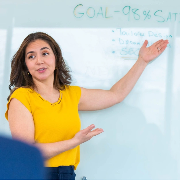 Woman presenting with a whiteboard that has goals for tailored designs - 98% satisfaction rate